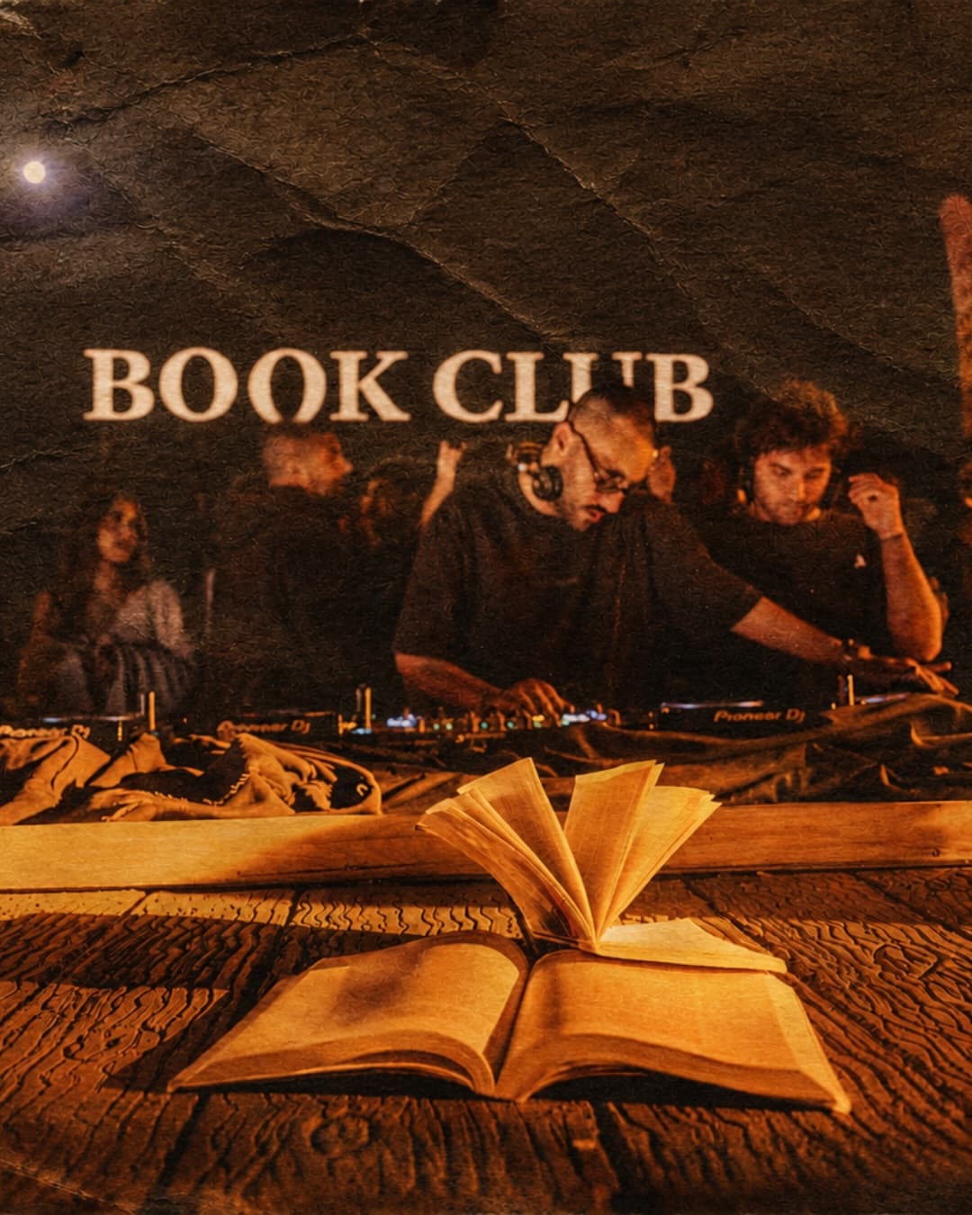 A glowing 'Book Club' sign above two DJs performing at a Book Club Only party, with an open book on a wooden table in the foreground