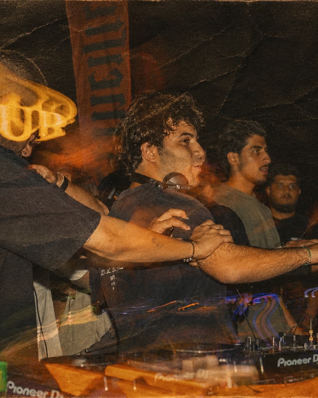 A group of Book Club Only guests with arms linked at the DJ booth, captured in a motion-blur double exposure