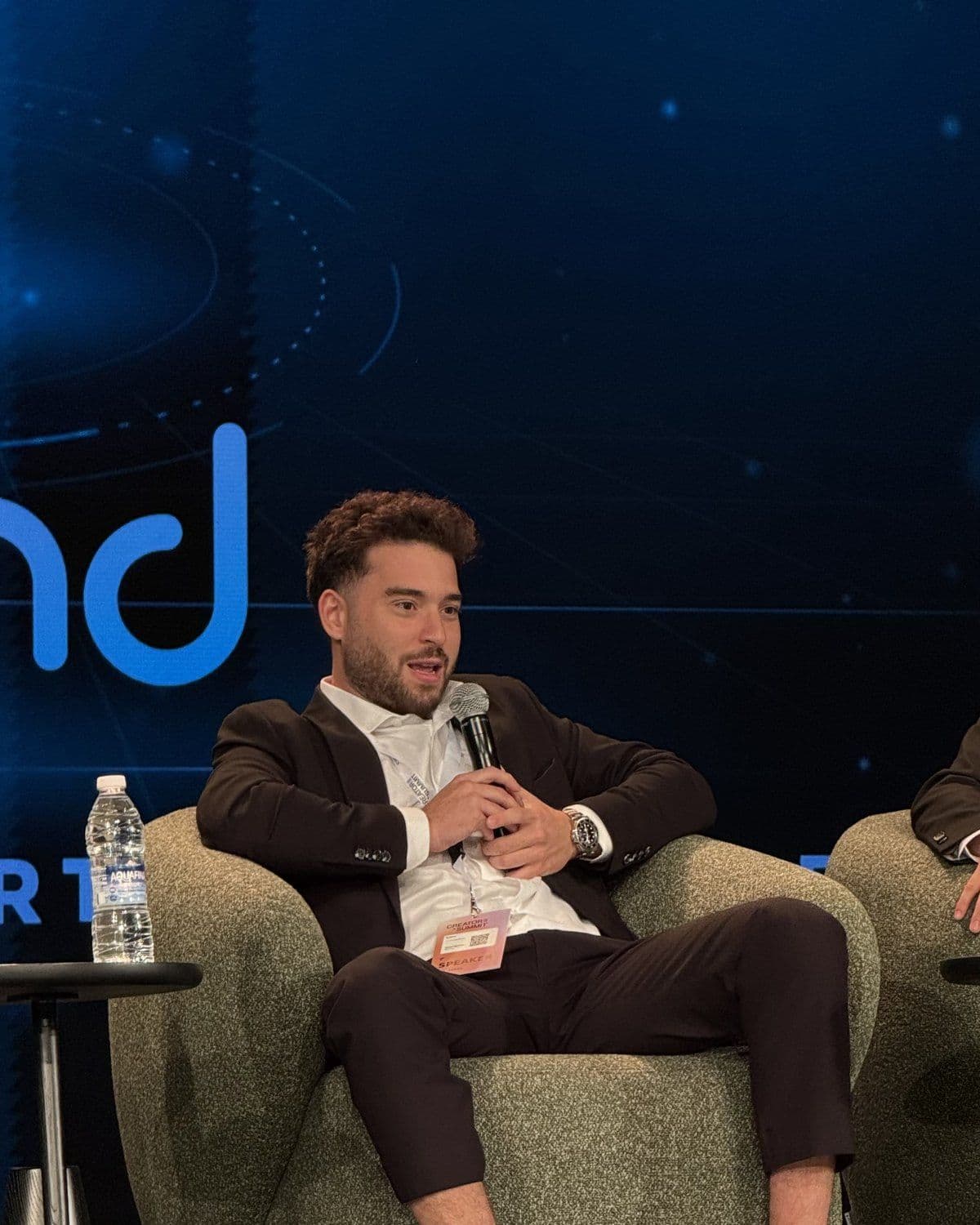 A panel speaker seated on stage, the Blend logo on the screen behind him