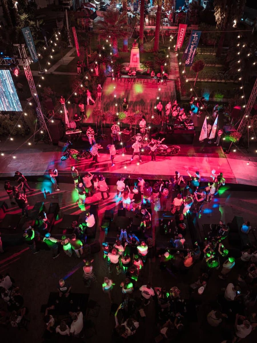 An aerial view of a live band performing on a pink-lit stage with a dancing crowd at Defile Classique