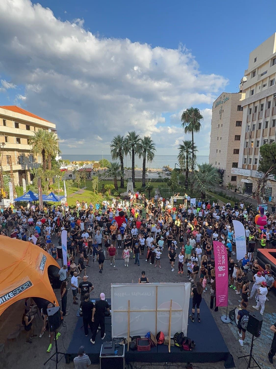 An elevated view of hundreds of runners gathered at the Run Fest 2026 start line on the Jounieh waterfront, palm trees and the sea in the background
