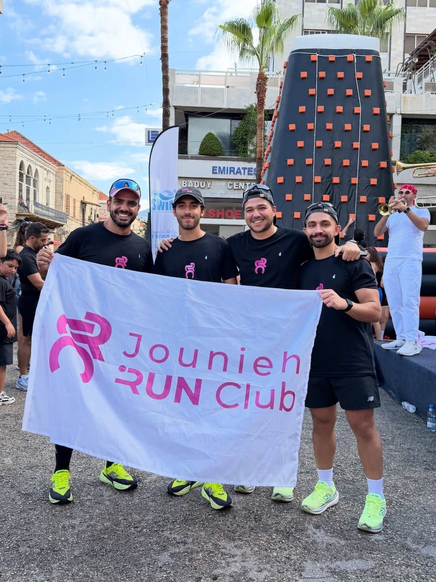 Four Jounieh Run Club members holding the club's pink-and-white flag in front of a climbing wall at Run Fest 2026