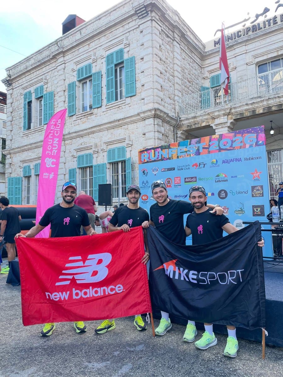Four runners holding New Balance and Mike Sport sponsor flags in front of the Run Fest 2026 backdrop outside Jounieh's municipality building