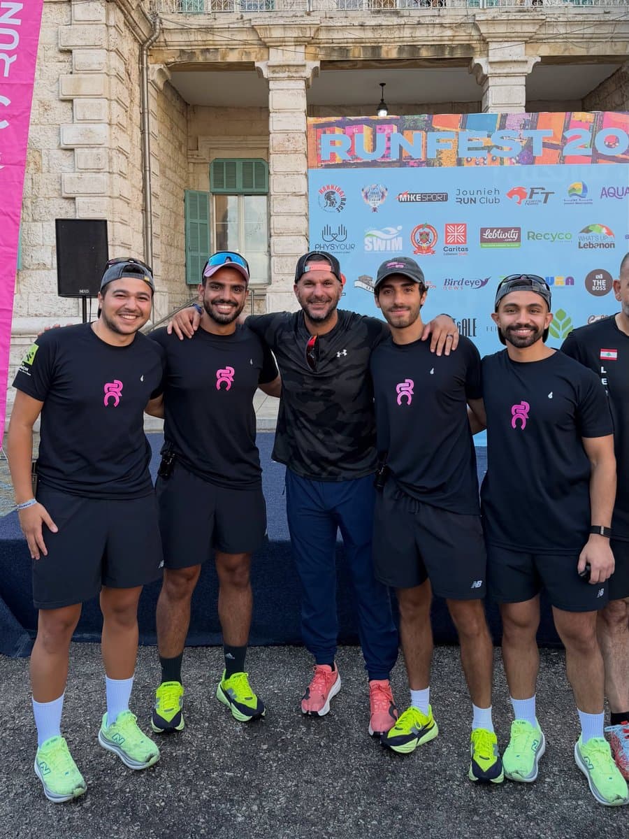 Five people posing together in front of the Run Fest 2026 sponsor wall, arms around each other