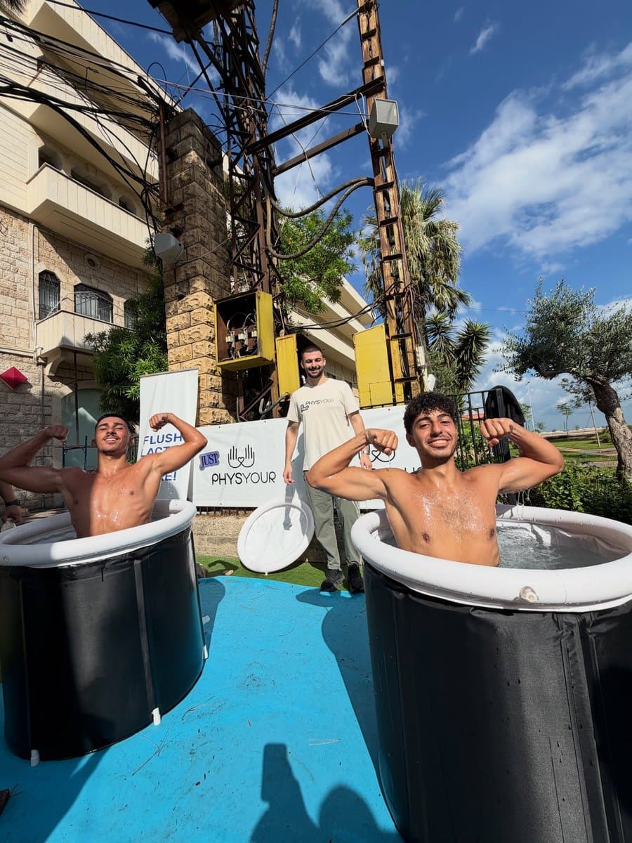 Two young men flexing inside cold-plunge ice bath tubs at a Physio Your recovery activation during Run Fest 2026