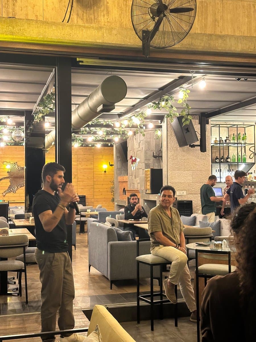 A man speaks into a microphone addressing a seated crowd at a Network With Jean networking event
