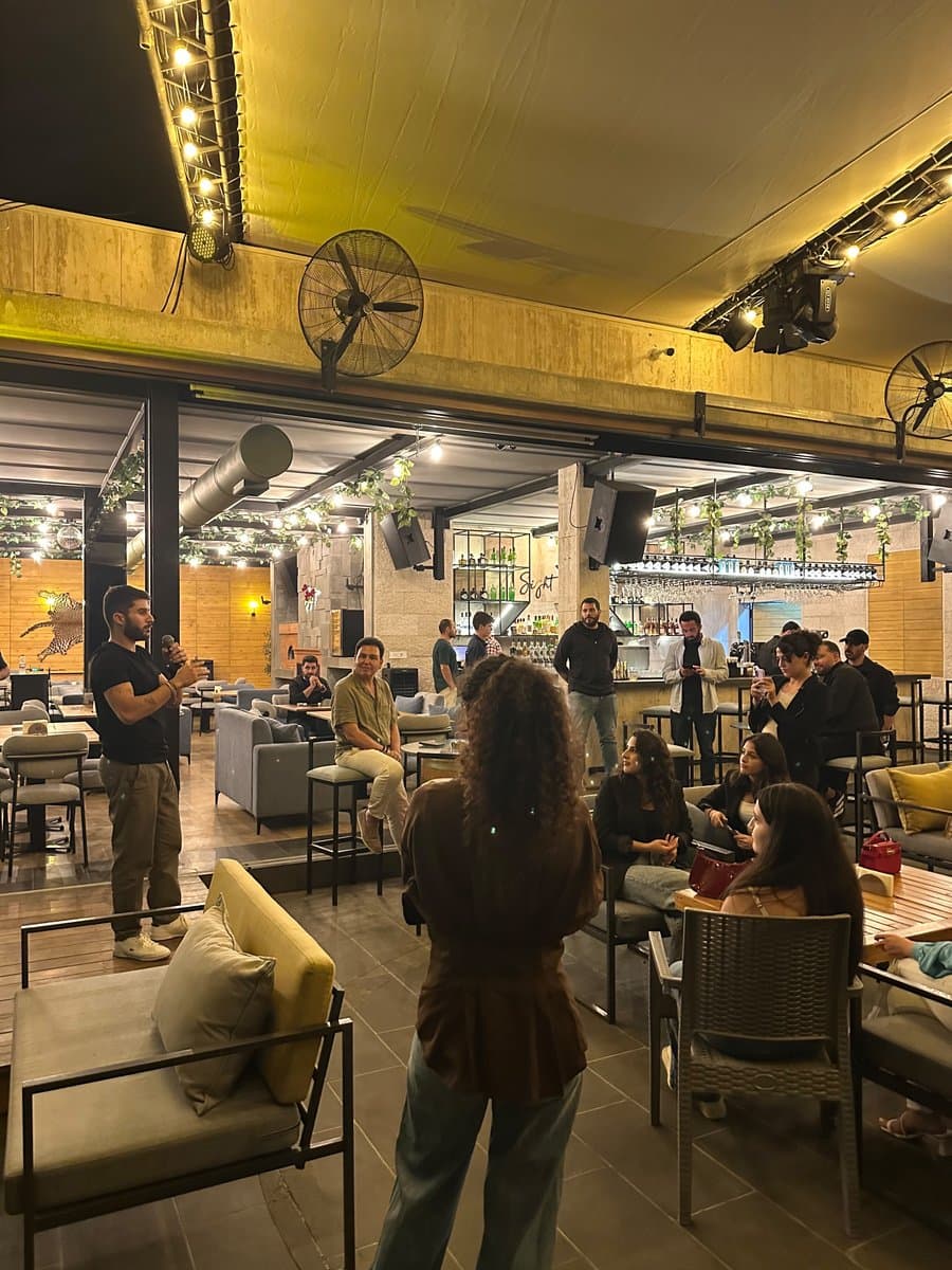 Guests seated around wooden tables under string lights and industrial fans at a Network With Jean rooftop networking event