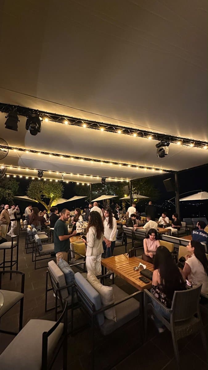Guests mingling on an open-air terrace with string lights and distant hillside views at dusk during Network With Jean