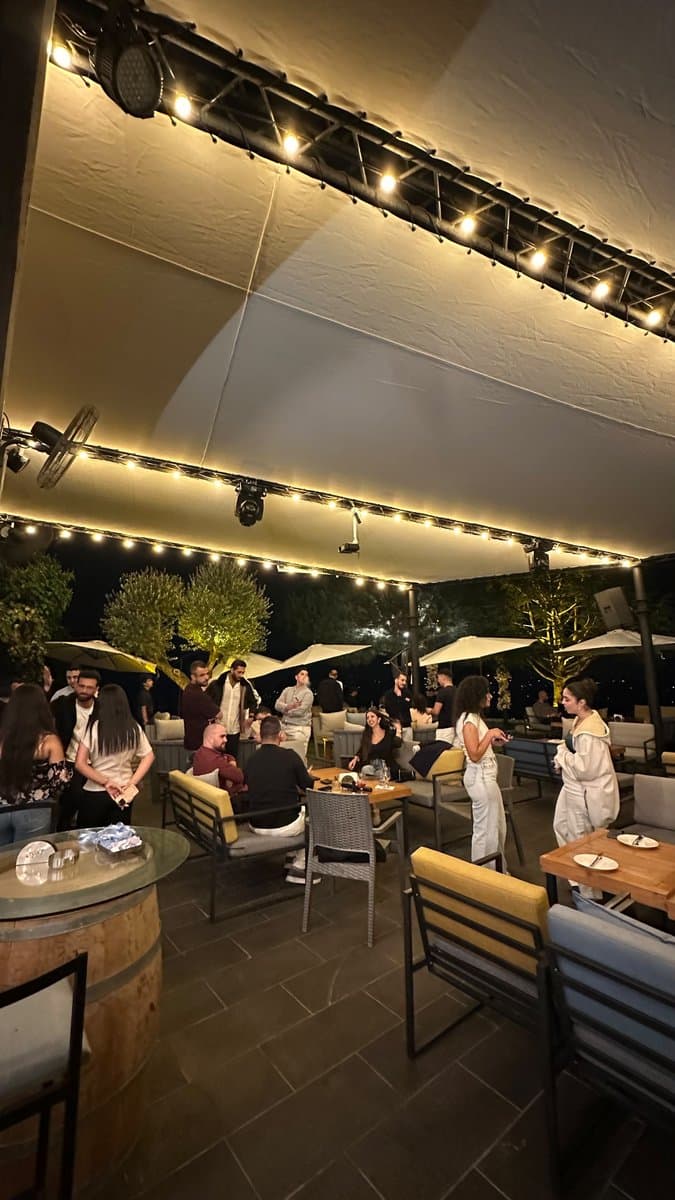 Guests gathered around a wine-barrel table on the terrace at Network With Jean, with string lights and umbrellas in the background