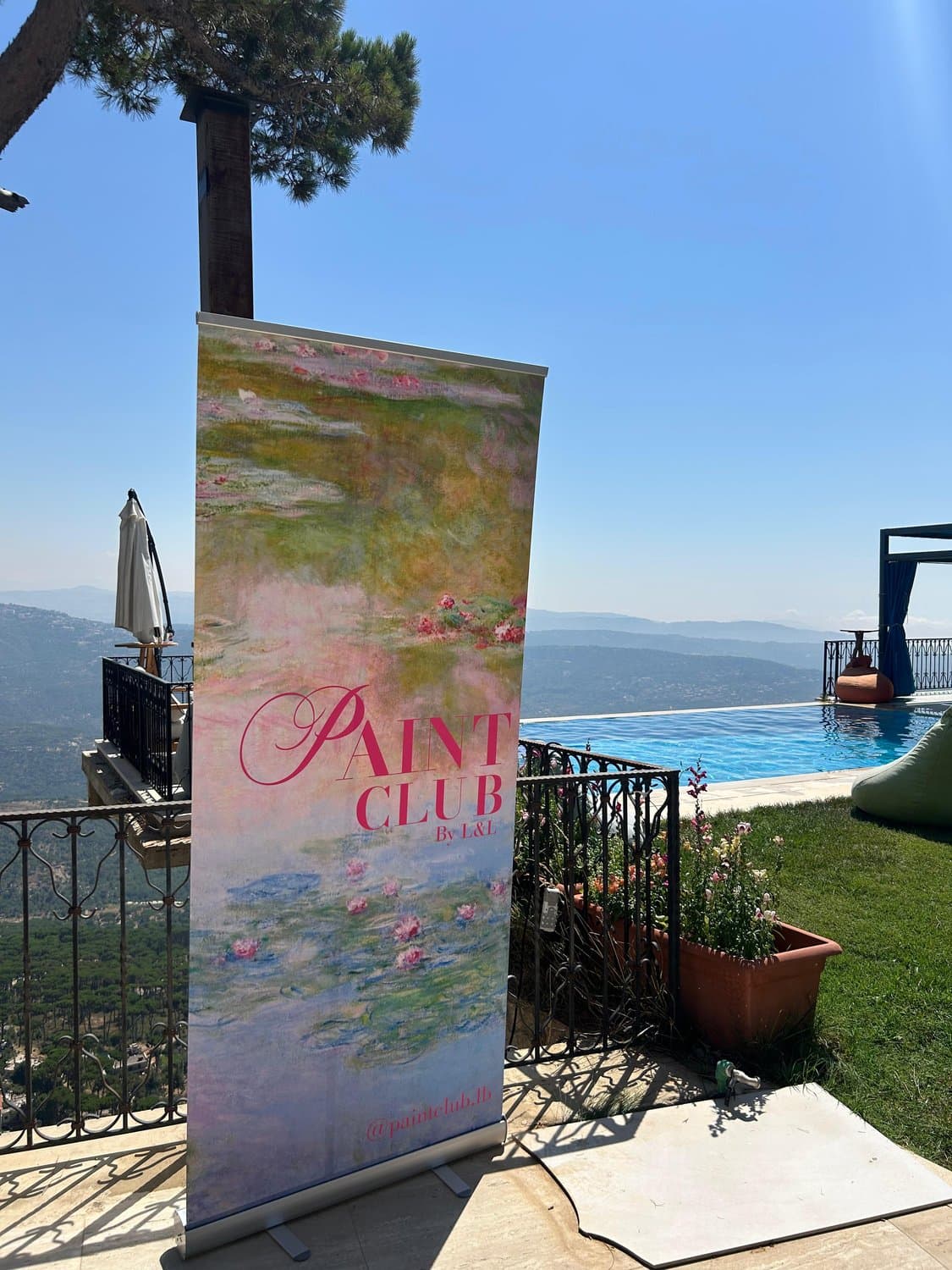 A Paint Club step-and-repeat banner in Monet water-lily style standing beside an infinity pool overlooking the mountains at Dhour El Choueir, Lebanon