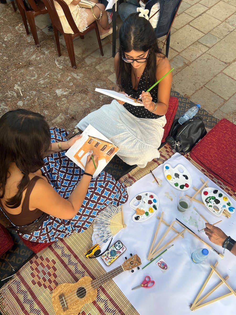 An overhead view of two people painting together, surrounded by a full spread of paint palettes, brushes and water cups