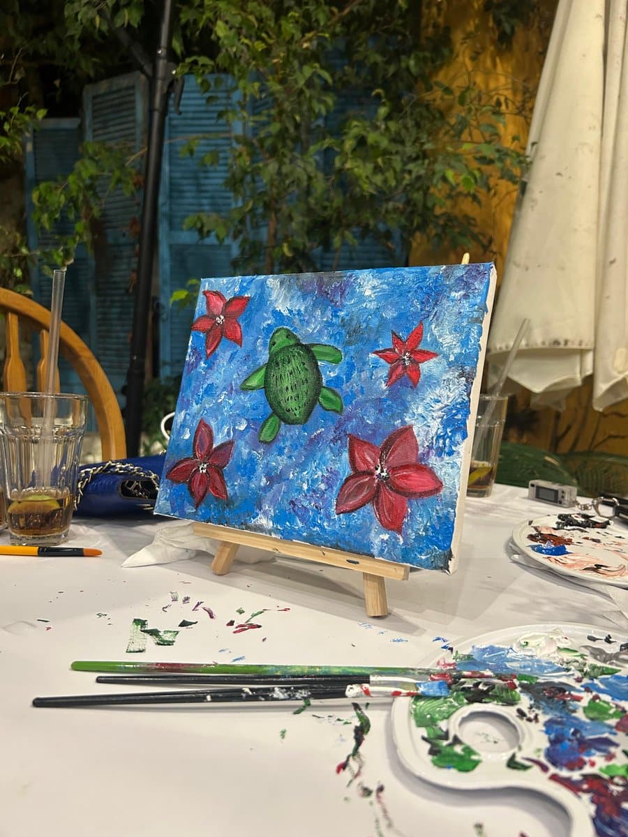 A finished painting of a sea turtle surrounded by coral-pink flowers, displayed on a small easel at a Paint Club session