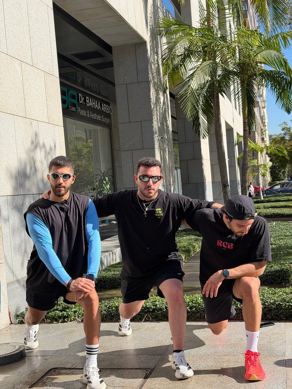 Three runners in sunglasses posing together in matching black outfits, one wearing a shirt reading 'RCB'