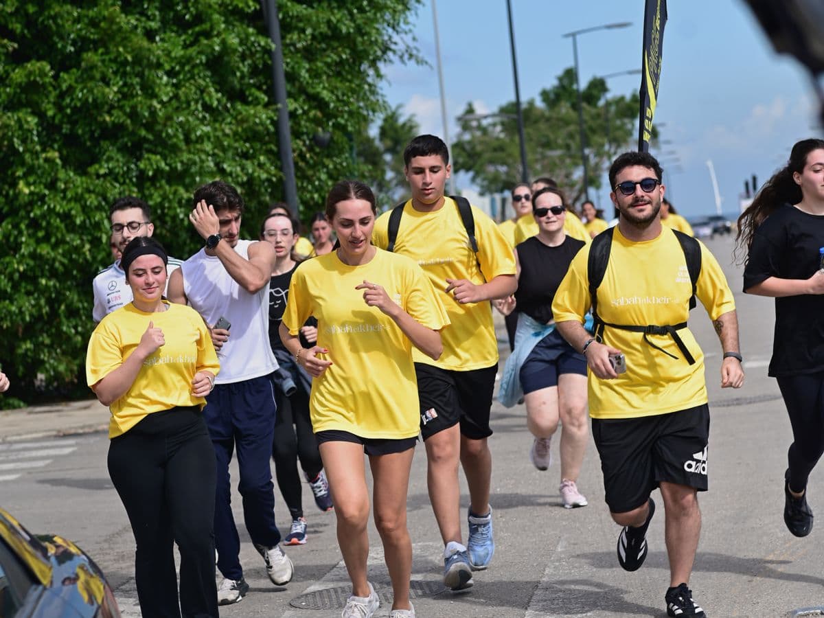 Runners in yellow Sabah El Kheir Run t-shirts jogging together along a tree-lined Beirut street