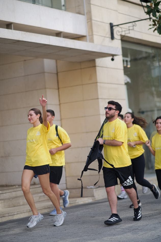 Runners wearing backpacks jogging past a row of storefronts in Beirut