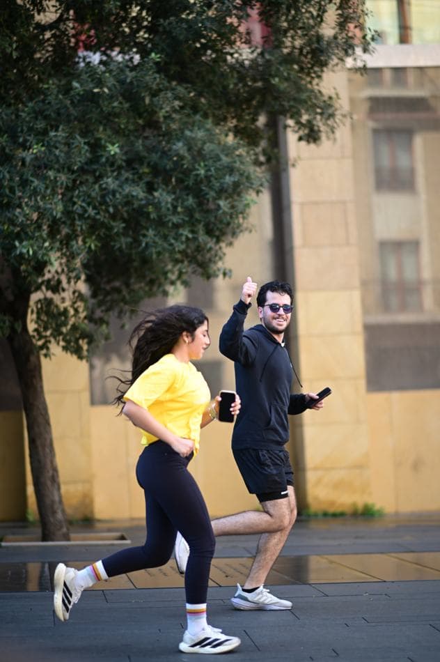 A man and woman running at pace along a Beirut street, one in a yellow Sabah El Kheir Run t-shirt