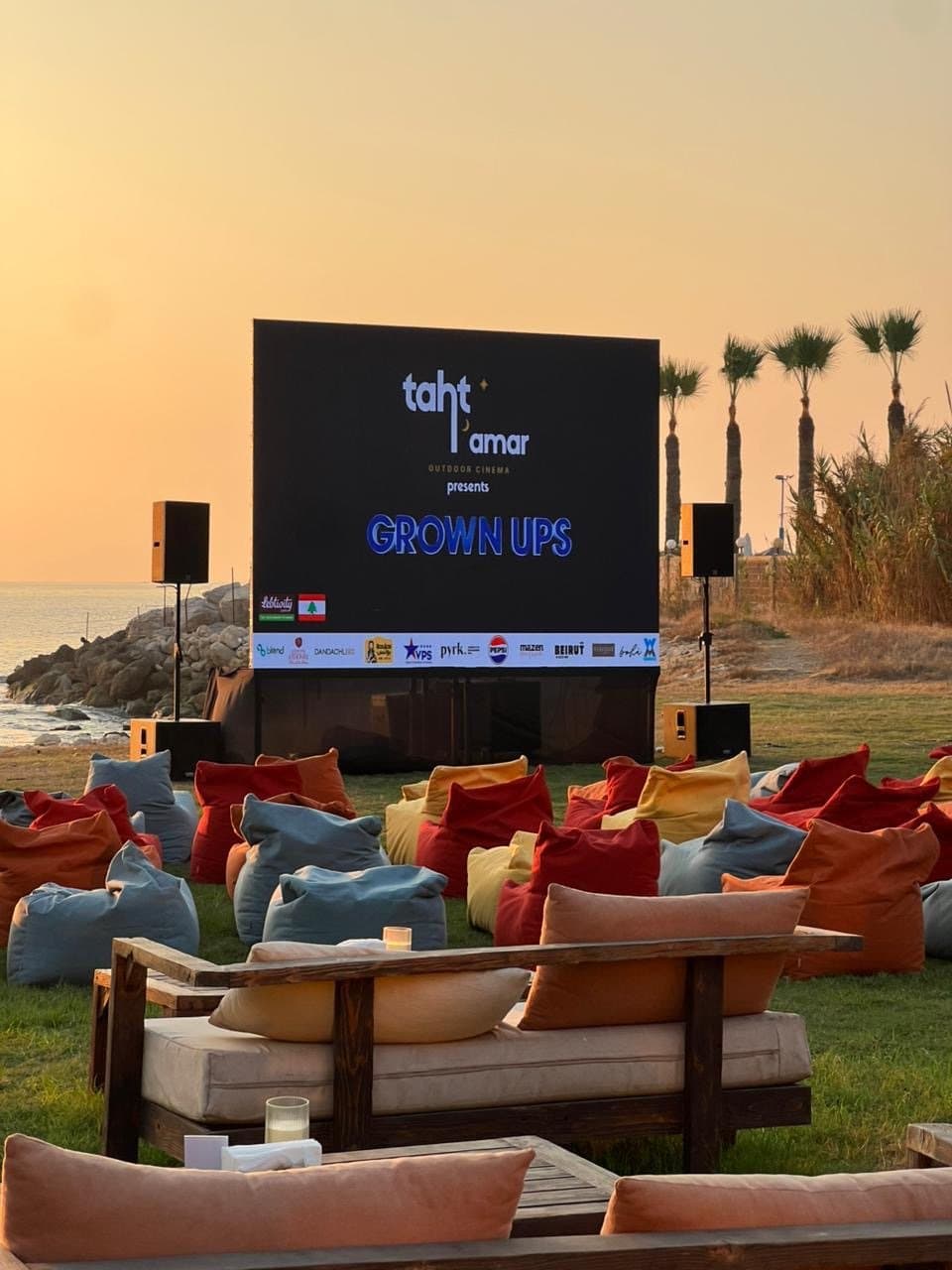 Taht El Amar's screen at sunset by the coast, with VIP lounge seating and beanbags facing it