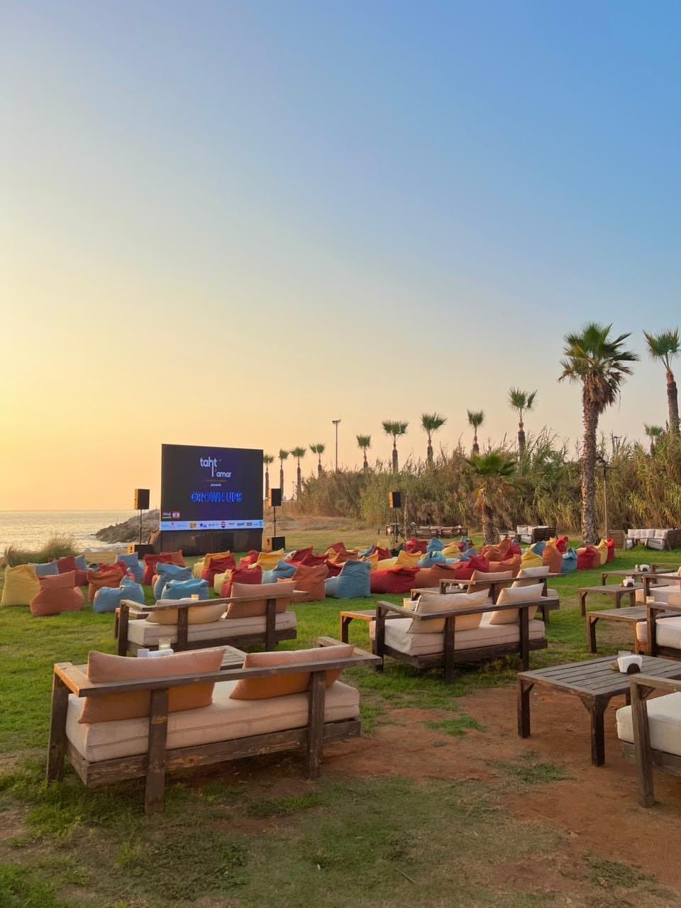 Beanbag seating and a VIP lounge sofa facing the Taht El Amar screen at dusk, overlooking the coast